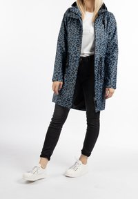 Imperméable à imprimé léopard aux tons bleus, doté d'une fermeture éclair, d'une capuche et de poches latérales. Associé à un jean skinny noir et des baskets blanches.