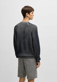 Marineblau gestreifter Strickpullover mit gerippten Bündchen und Saum, kombiniert mit grauen, strukturierten Shorts. Sichtbare Nahtdetails und eine lockere Passform.