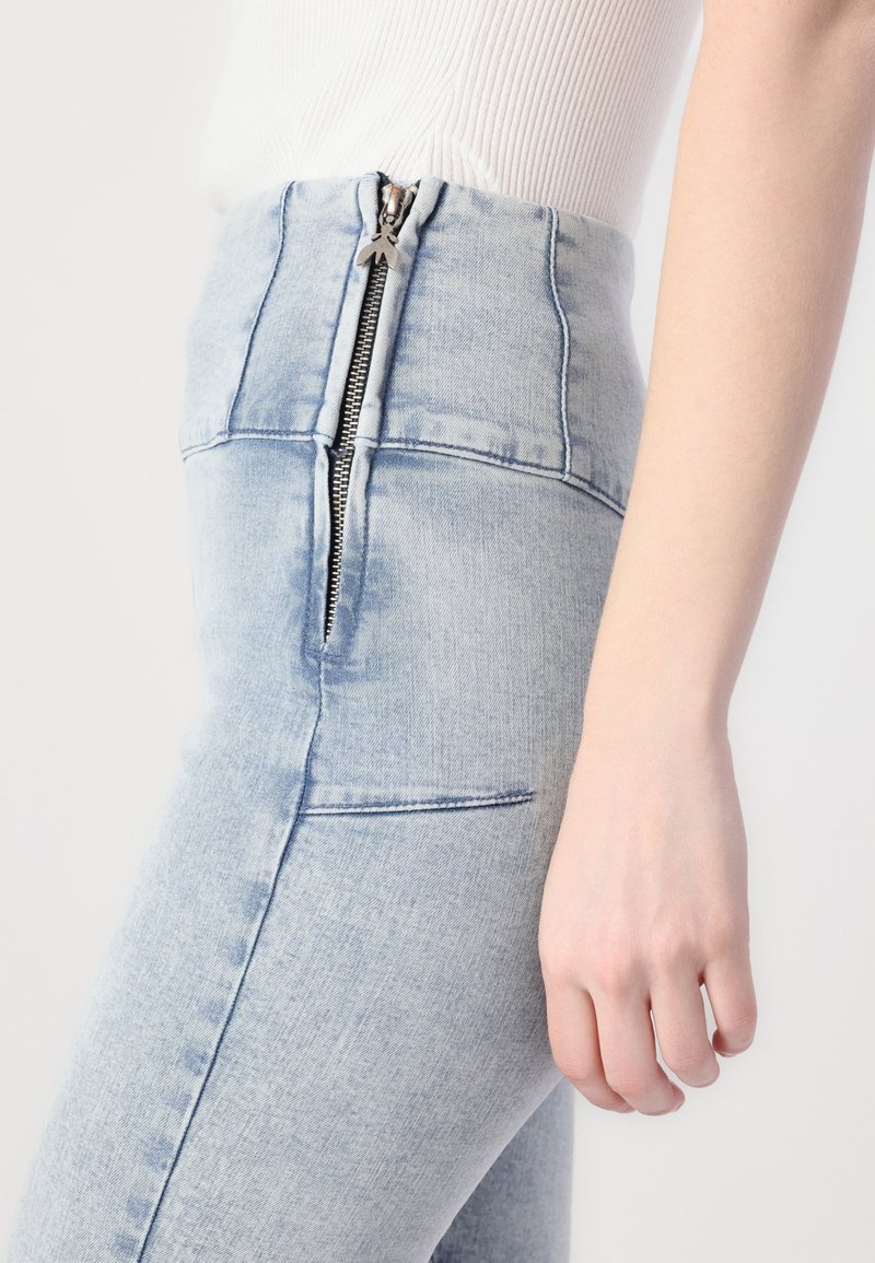 Jasnoniebieskie dżinsy z wysokim stanem z metalowym zamkiem z przodu, charakteryzujące się gładką teksturą i kieszeniami po bokach.