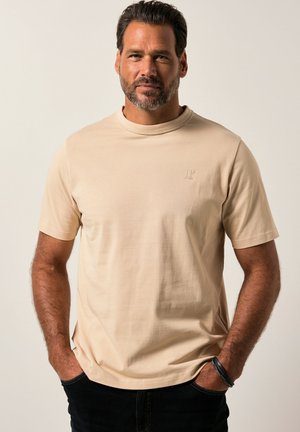 Camiseta de manga corta beige hecha de tela suave, con un escote redondo y un sutil logo en relieve en el pecho. Diseño sencillo, ajuste relajado.