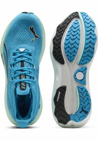 Zapatillas deportivas azul claro con parte superior de textil, acentos en negro y blanco, patrones de relieve prominentes en la suela de goma y cordones.