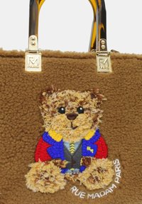 Borsa a tracolla in peluche marrone con ricamo di un orsetto che indossa un abito multicolore, dotata di accessori in oro e dettagli con logo.
