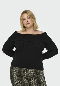 Zwarte geribbelde off-shoulder trui met lange mouwen en een brede halslijn, gecombineerd met metallic legging met luipaardprint.