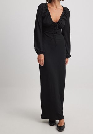 Vestido negro de manga larga con escote en V profundo, ribete con volantes y detalle de cordón. Presenta una silueta ajustada y tela texturizada.