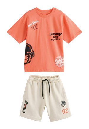 Koraalrood katoenen t-shirt met zwarte grafische prints, waaronder een gorilla en tekst, gecombineerd met beige shorts met zwarte trekkoord en printdetails.