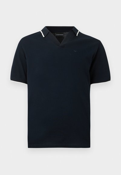 Μπλε ναυτικό κοντομάνικο πόλο με λευκή επένδυση στη γιακά και στις άκρες των μανικιών, με V-λαιμόκοψη και διακριτικό λογότυπο στο στήθος.