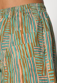 Pantalones cortos de algodón con una paleta de colores pasteles que presentan patrones abstractos a rayas en turquesa, marrón y melocotón. Cintura elástica para mayor comodidad.