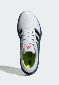 Zapatilla deportiva blanca con rayas negras, parte superior de malla, suela de goma y un interior de neón brillante. Presenta cordones planos y un logo en la lengüeta.