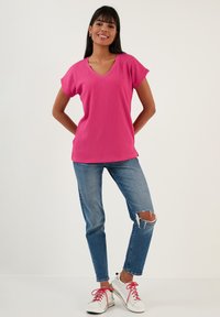 Fuchsia V-neck top with short sleeves, textured fabric; paired with light blue ripped jeans and white sneakers with pink laces.