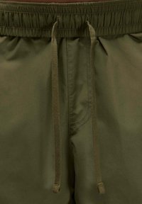 Shorts oliivivärvi, valmistettu kevyestä kankaasta, jossa on joustava vyötärö, jossa on nyörit, sekä ommellut yksityiskohdat saumoissa.