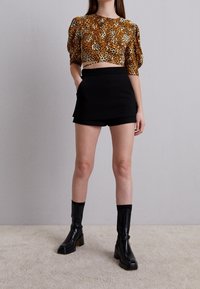 Top court en imprimé léopard aux tonalités oranges et brunes, associé à une mini-jupe noire taille haute et des bottes noires à talons hauts montantes.