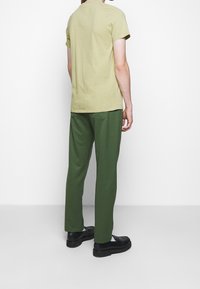 Ljusgrön kortärmad t-shirt i kombination med mörkgröna byxor, kompletterad med svarta slip-on skor. Enkel design, avslappnad passform.