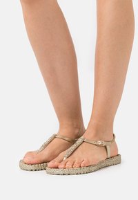Sandali espadrille beige con suola texturizzata, dotati di un cinturino decorativo arricchito da strass trasparenti e chiusura a fibbia.