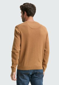 Brauner Strickpullover mit Rundhalsausschnitt, enganliegenden Bündchen und Bund. Über blauen Denim-Jeans getragen, was eine glatte Textur zeigt.