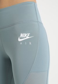 Leggings azul claro con una textura suave, que presentan un logo blanco de Nike y el texto "AIR". Incluyen un panel con franjas horizontales.