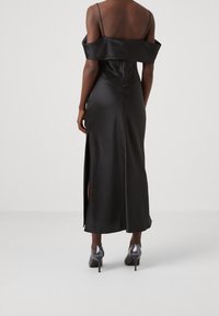 Svart satin off-shoulder klänning med åtsittande liv, sidoflikar och ankellång längd, i kombination med blanka klackskor.