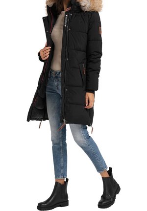 Woman wearing a long black puffer coat with fur hood, beige ribbed sweater, blue jeans, and black ankle boots, standing with one leg bent.