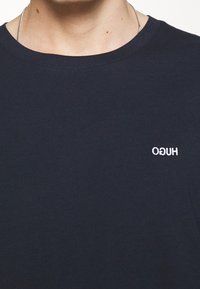 Navyblaues Baumwoll-T-Shirt mit Rundhalsausschnitt und kurzen Ärmeln. Mit dezentem weißen "HUGO"-Logo, das auf der linken Brustseite gestickt ist.