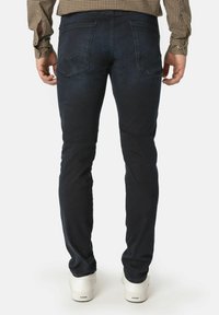 Smal passform mørkeblå jeans med en glatt tekstur, med to baklommer og minimale sømdetaljer, sammen med hvite sneakers.