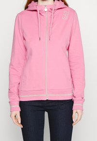 Rosa zip-up hoodie i mjukt material, med en dragsko i huvan, silverdetaljer på ärmsluten och nederkanten. Logotypen syns uppe till vänster.