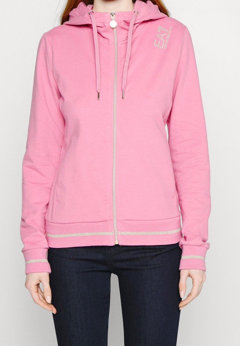 Rosa zip-up hoodie i mjukt material, med en dragsko i huvan, silverdetaljer på ärmsluten och nederkanten. Logotypen syns uppe till vänster.