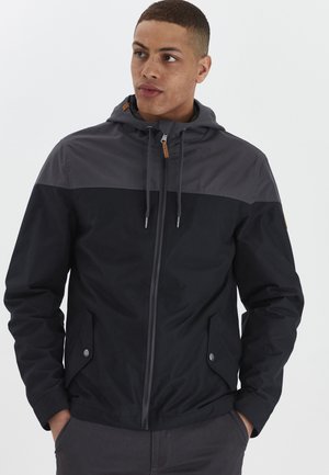 Black and gray jacket featuring a zippered front, hood, and side pockets. Made of lightweight material with a smooth texture.