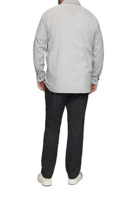 Chemise à rayures à manches longues en gris clair et marine, avec des poignets à boutons et une coupe décontractée. Associée à un pantalon sombre et des chaussures blanches.