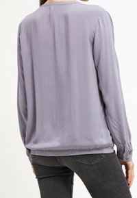 Blouse à manches longues en satin gris clair, avec un col rond, des épaules froncées et un ourlet élastique pour un look ajusté.