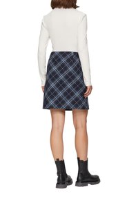 Granatowa spódnica w kratę z niebieskimi liniami, płaski pas, długość powyżej kolan, zestawiona z dopasowaną białą bluzką z długim rękawem i czarnymi botkami za kostkę.