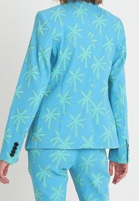 Niebieski garnitur z długimi rękawami i spodniami, ozdobiony wzorem z jasnych zielonych palm, widziany od tyłu.