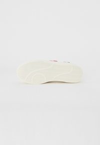 Semelle de sneaker blanche avec un motif en vagues et des accents colorés, présentant des designs rouges et verts. Matériau en caoutchouc lisse.