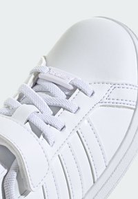 Baskets blanches avec une tige en cuir lisse, accents texturés et lacets plats. Équipées d'une sangle à crochets et d'une discrète détail de logo.