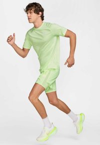 Neon grøn atletisk t-shirt og shorts med struktureret design. Hvide sko med neonlys. Glat stof, let udseende.