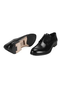 Chaussures habillées en cuir noir avec une finition lisse, bout rond et lacets. La semelle est un mélange de noir et de tan avec un léger talon.