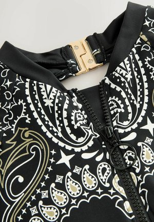Črna kopalna obleka s zlatim in belim paisley vzorcem. Ima sprednji zadrgo s črnim oblačkom in zlatim zapiranjem pri ovratniku.