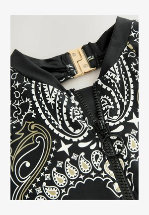 Črna kopalna obleka s zlatim in belim paisley vzorcem. Ima sprednji zadrgo s črnim oblačkom in zlatim zapiranjem pri ovratniku.