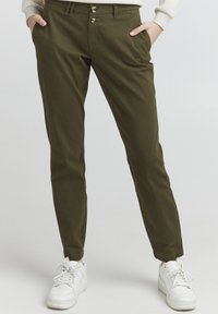 Olive green pants in a slim fit, made of soft cotton material. Features two front pockets and a double-button closure. Paired with white sneakers.