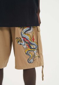 Tan cargo kraťasy s barevným výšivkovým designem draka v modré, červené a žluté barvě, mají kapsy a stahovací šňůrku na lemu.