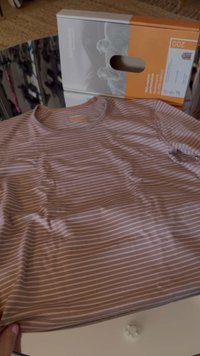 Light pink and white striped shirt, round neck, soft fabric with slight wrinkles, laid flat on a table next to a partially visible product box.