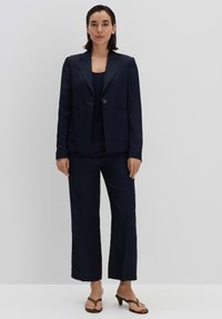 Costume en lin bleu marine avec une veste cintrée dotée de deux poches avant et d'un bouton unique, associée à un pantalon à jambes droites.