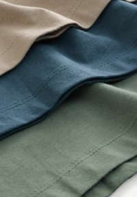 Tre lager av tyg i beige, mörk teal och olivgrön; alla är släta bomullstyger med synliga sömmar längs kanterna.