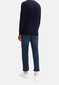 Granatowy sweter z detalem na szwie tylnym, połączony z jasnoniebieskimi dżinsami i białymi sneakersami. Sweter ma długie rękawy i luźny krój.