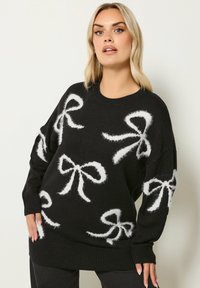 Czarny sweter z dużymi białymi, futrzastymi wzorami w kształcie kokard. Projekt obejmuje okrągły dekolt oraz ściągacze, a także luźny krój.
