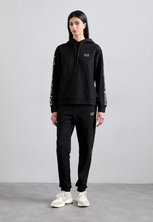 Zwarte hoodie met logo, kangoeroezak en trekkoord. Gecombineerd met zwarte joggers met logo-accenten. Beide gemaakt van zachte stof.