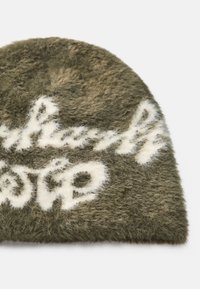 Olivgrüne Mütze aus flauschigem Material, mit weißer Schrift in einem sanften, texturierten Design. Runde Form mit einem leicht gewellten Rand.