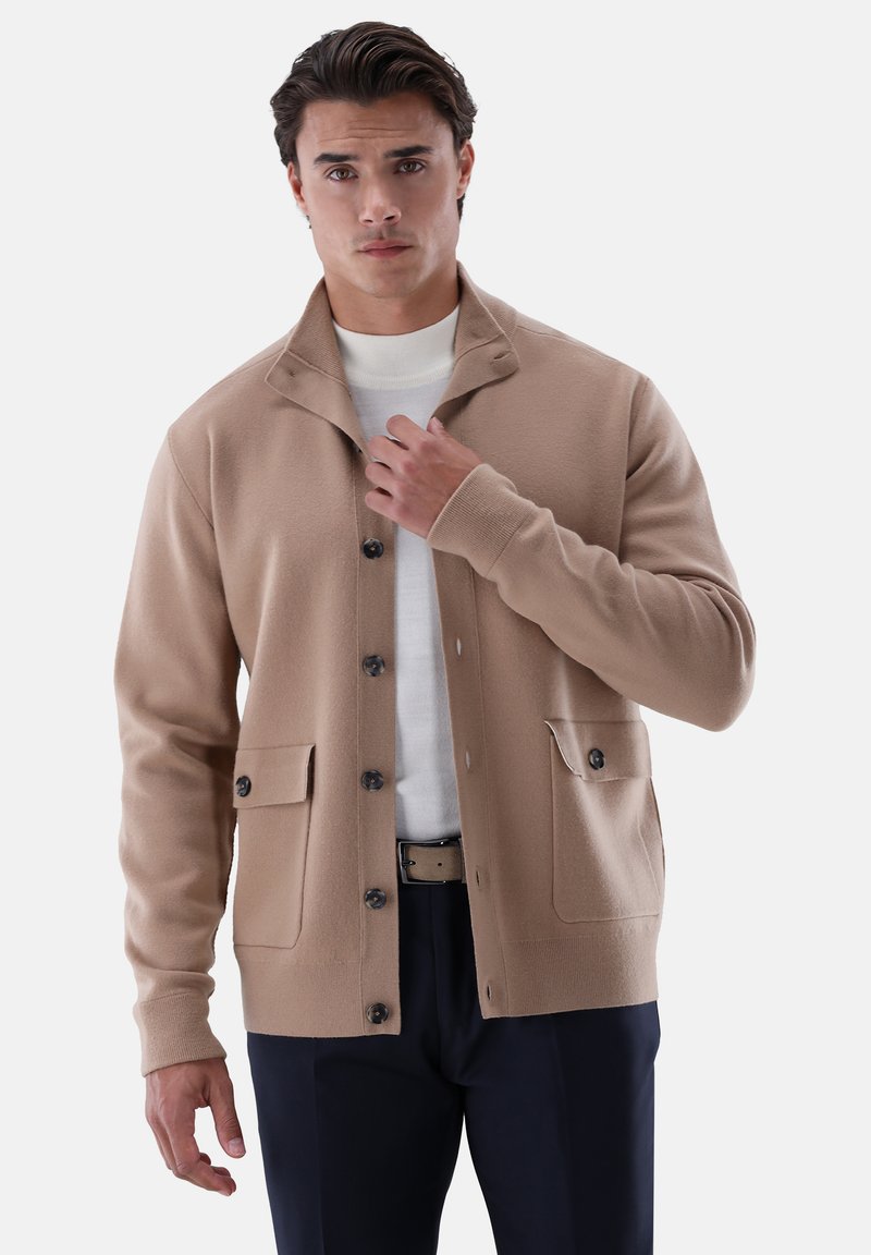 Beiger Cardigan mit hohem Kragen, Knopfleiste vorne, zwei Eingrifftaschen und langen Ärmeln; hergestellt aus weichem Material mit glatter Textur.