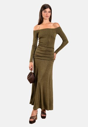 Olivgrünes, schulterfreies Kleid aus strukturiertem, glitzerndem Stoff mit Raffung, langen Ärmeln und weitem Saum. Kombiniert mit einer braunen Tasche.