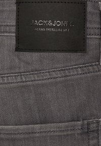 Ciemnoszare dżinsy denimowe z czarną skórzaną naszywką z wypukłym napisem. Szwy przy kieszeniach, gładka faktura i klasyczny design.