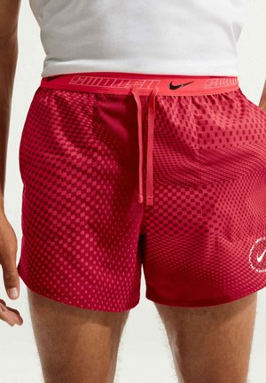 Man draagt rode geruite Nike sportshorts met "SWOOSH" tailleband en trekkoord, gecombineerd met een wit mouwloos shirt.
