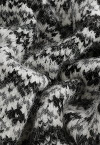 Tissu tricoté présentant un motif pied-de-poule noir et blanc, avec une surface douce et texturée et des fibres lâches et duveteuses.